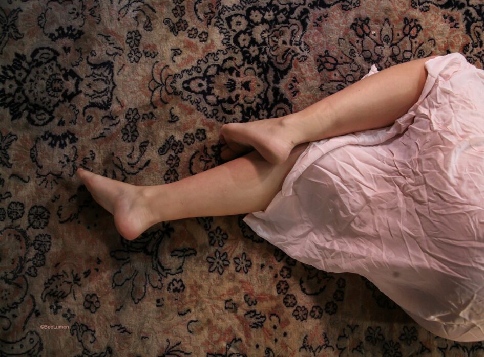 Les jambes d'une femme émerge sous une jupe blanche, allongeées suer un tapis aux motifs fleuris
